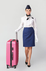 Beautiful stewardess with luggage on grey background