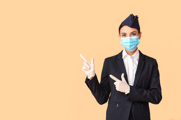 Beautiful stewardess in medical mask showing something on color background