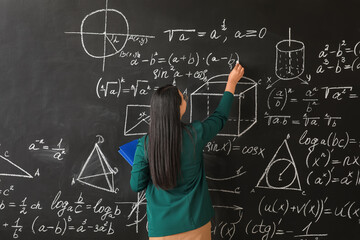 Asian female teacher writing on blackboard in classroom