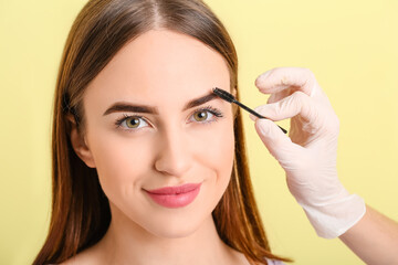 Fototapeta premium Young woman undergoing eyebrow correction procedure on color background