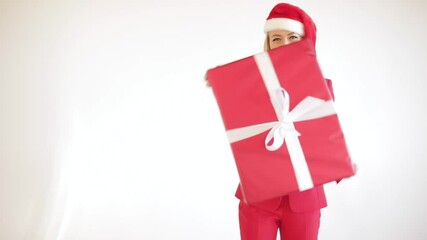 Stock video of cheerful attractive woman with red lips and red Santa hat and red suit rotating red Christmas gift with bow. - Powered by Adobe