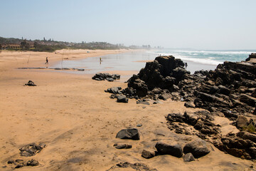 Black Rocks on Beach with Fishermen in Background