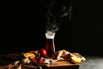 Glass of tasty pomegranate cocktail on table against dark background