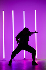 Fototapeta na wymiar Young woman dancing street dance hip hop in a studio with neon lighting tube on a purple background. Dark silhouette. Dance and music poster design.