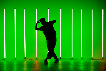 Fototapeta na wymiar Silhouette of man giving solo performance in hip hop style on club scene with green background neon lamps. Close up. Dance school poster.