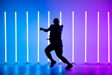 Young breakdancer guy dancing hip-hop in colorful neon background with neon lamps. Breakdance lessons. Close up.