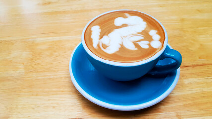 Close up blue cup of art cappuccino or latte coffee on brown wooden background with copy space. Flat lay of hot drinking in the morning at cafe shop. Food design concept.