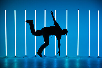 Full size of silhouette of male break dancer performing on blue neon stage acrobatic jumping....