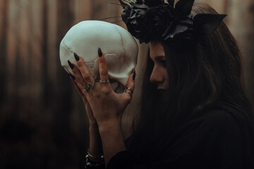 portrait of a terrible witch with a skull in the hands of a dead man performs an occult mystical...