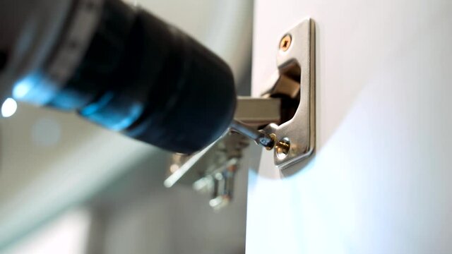 The cabinet maker tightens the adjustment screw on the cabinet door hinge in the kitchen. Installation and adjustment of cabinet doors.
