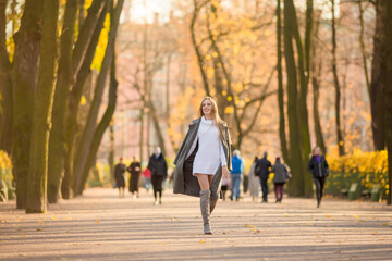 Obraz premium Happy young woman walks in the autumn park. An attractive woman with light brown hair and a gray coat is walking down the alley. Beautiful autumn mood. Fall season.
