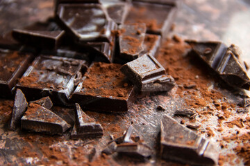 Dark chocolate bar with chocolate pieces with cocoa powder on brown background, close-up view