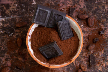 Bitter chocolate in a clay cup with cocoa on a blurred background, top view