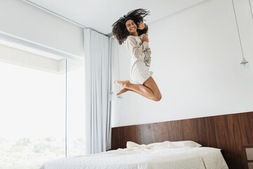 curly hair latin american woman jumping on bed listen music