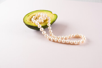 half an avocado with pearls on a light pink background. surrealism. Fashionable food design.