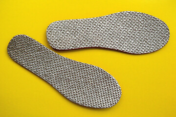 Two shiny insoles for shoes on a yellow background