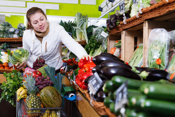 Obraz premium Satisfied young woman doing shopping in store of fruits and vegetables