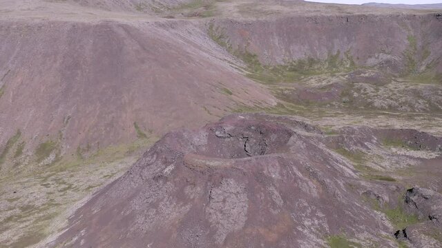 Aerial flying towards old volcanic crater consisting of scoria rock