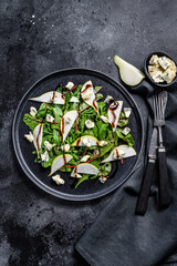 Pear, blue cheese, arugula and nut salad on plate. Black background. Top view