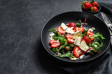 Brie cheese salad with strawberries, nuts, chard and arugula. Black background. Top view. Copy space