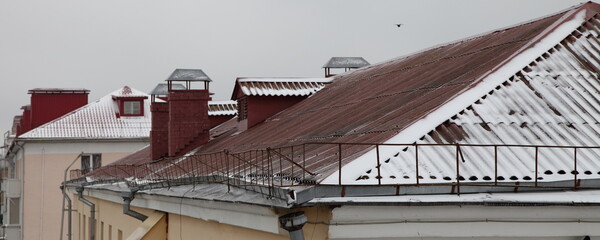 Snow covered old red tiled house roofs against a gray sky, European winter landscape