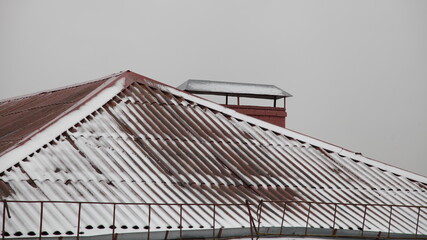 Snow covered old red tiled house roof on gray sky background, European winter landscape