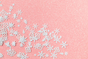 Light pink background with glitter and sequins in the form of white snowflakes and Christmas trees. Flat lay design