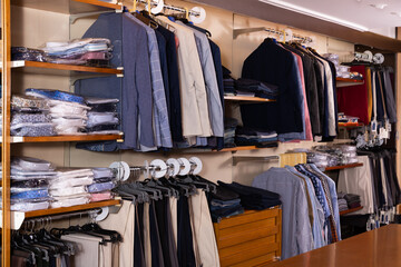 Men clothing store with variety of suit coats, dress pants, shirts on display.