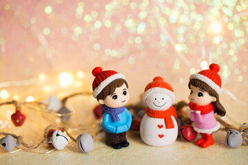 Winter Christmas background with toy figures of a girl and a boy who make a snowman. Joyful and positive children's Christmas background with shiny elements and decorations.