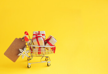 Christmas, New Year and winter sale concept. Shopping cart with gift boxes and blank label for inscription on yellow background with copy space. - 393507471