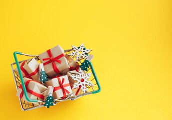 Christmas gifts and New Year decorations in a shopping basket on yellow background with copy space. - 393507488