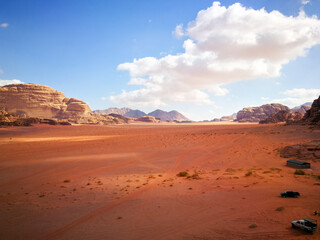 the red desert of Wadi Ram, relief mountains are on the horizon, beautiful clouds in the blue sky, contrasting shadows on the ground