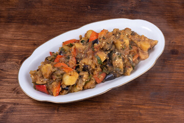 Traditional Italian vegetable stew with potatoes, eggplants, tomatoes and peppers in an oval plate on a woody background - Neapolitan style cianfotta.
