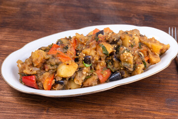 Traditional Italian vegetable stew with potatoes, eggplants, tomatoes and peppers in an oval plate on a woody background - Neapolitan style cianfotta.