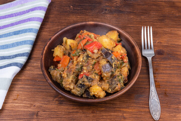 Traditional Italian vegetable stew with potatoes, eggplants, tomatoes and peppers in a rustic earthen plate on a rustic background - Neapolitan style cianfotta.