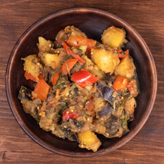 Traditional Italian vegetable stew with potatoes, eggplants, tomatoes and peppers in a rustic earthen plate on a rustic background - Neapolitan style cianfotta.
