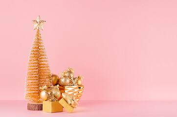 Gold christmas tree with sparkle stars, balls in bowl, gift box on elegant pastel pink background.