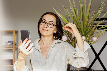Brunette woman decorates a palm tree like a Christmas tree and takes selfies. Alternative, eco...