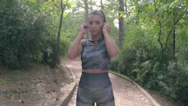 Girl listening to music on headphones while running. Young woman puts on airpods when exercising in nature.