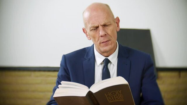 A professional businessman is reading the Holy Bible at home. The religious man is exploring his spirituality. Her reads and turns the pages deep in thought.