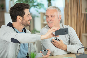 Obraz premium happy bearded son taking selfie with retired cheerful father
