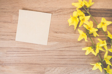 High angle shot of forsythia flowers and a piece of paper on a wooden surface