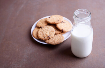 Fresh delicious milk in a glass bottle on a textured background with chocolate cookies on a white plate.
