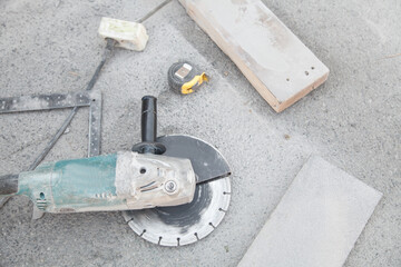 Angle grinder, stone, measuring roller on asphalt background.