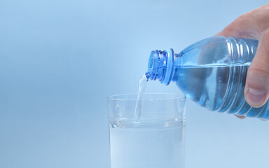 Male hand holding water bottle pouring water into glass.