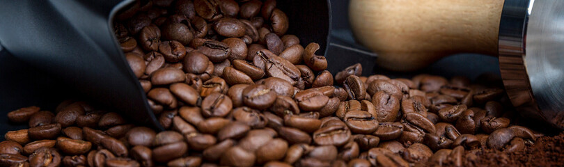 Scattered coffee beans on a black background. Close-up. Panorama format.