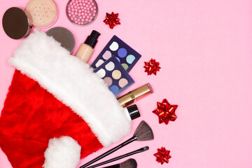 Makeup products with Santa hat and gift bows on pink background. Top view, copy space. Make-up cosmetics as Christmas and New Year present concept