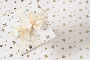 Gift box with beige bow on a light background with stars. Flat lay with soft focus.