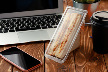 Triangle sandwich on wooden office table with laptop and coffee cup