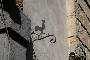 rooster made of plate iron on a sign board on an old stone wall